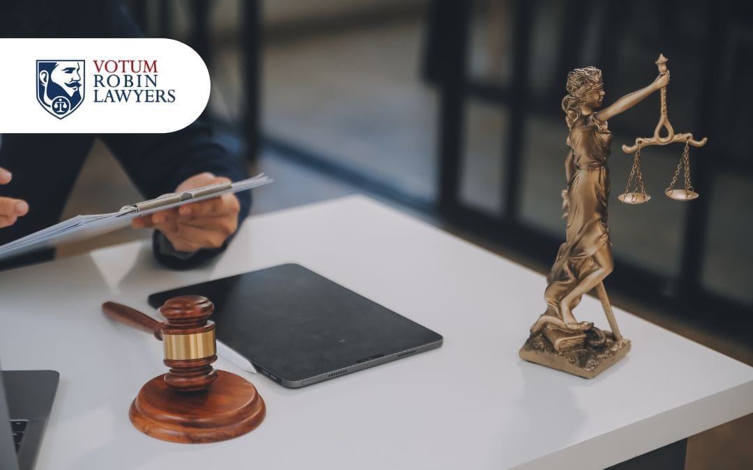 Prawnik analizujący dokumenty przy biurku, obok młotek sędziowski i figura Temidy – kancelaria Votum Robin Lawyers.