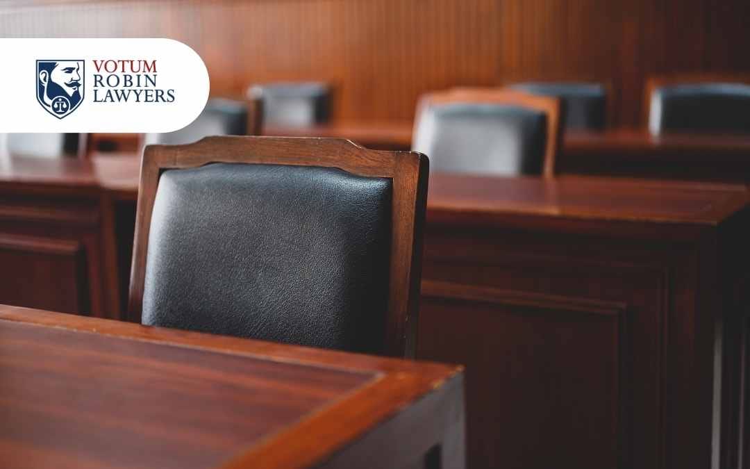 Prawnik podpisujący dokumenty przy biurku, obok młotek sędziowski i waga sprawiedliwości.
