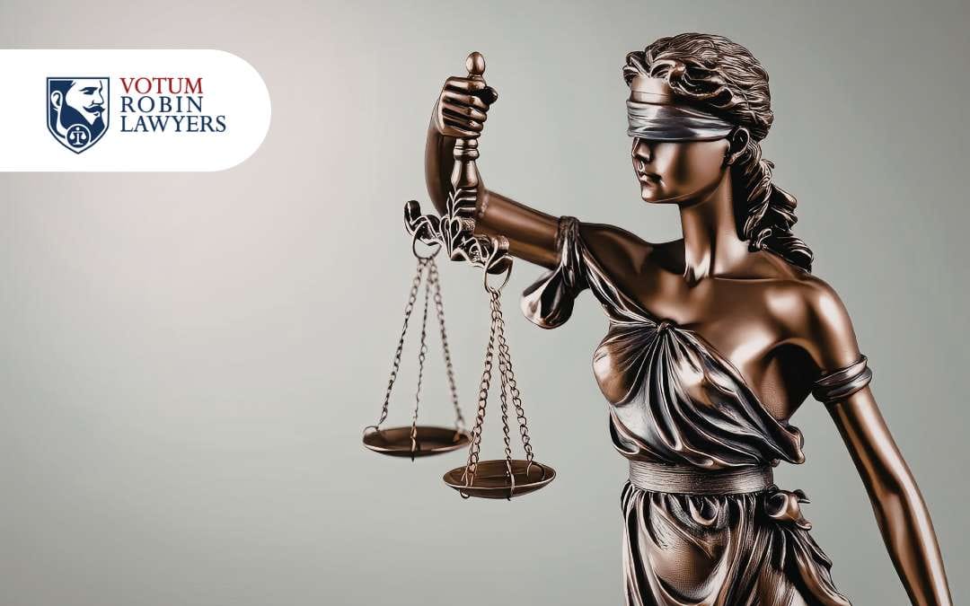 Statue of Lady Justice blindfolded, holding balanced scales, with the Votum Robin Lawyers logo in the top-left corner.