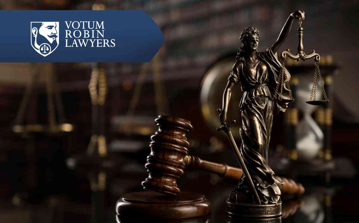 Lawyer's desk with hands typing on a laptop, a mobile phone nearby, gold scales and a gavel on the table, logo reading 'Votum Robin Lawyers' in the corner