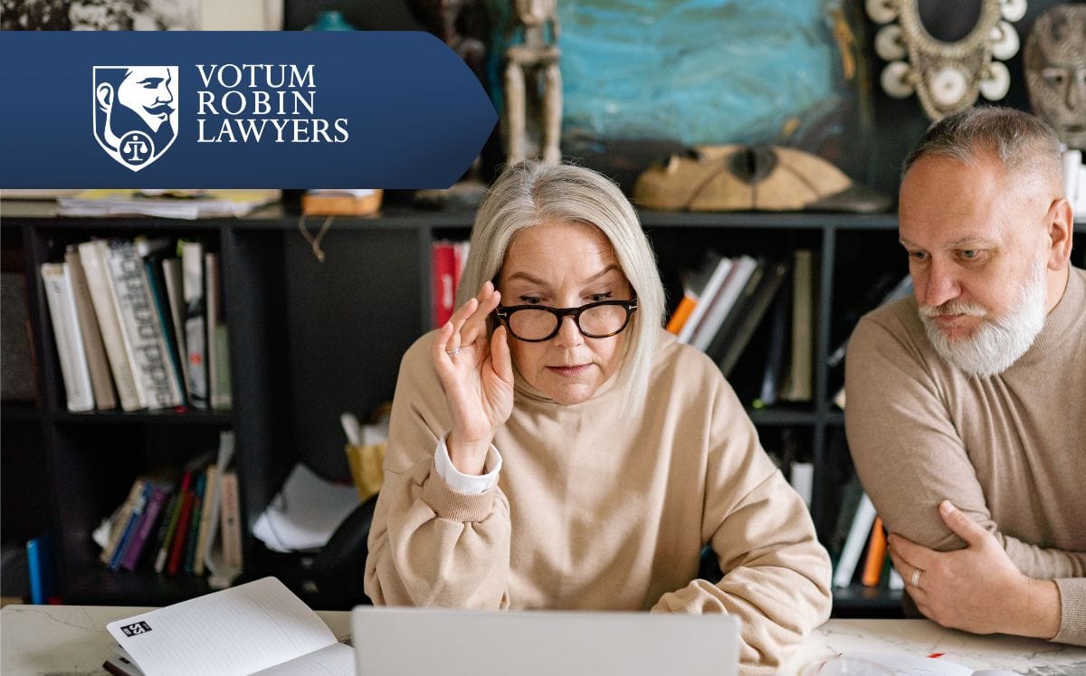 Two lawyers in suits review documents on a desk with a gavel and scales of justice; law firm logo in the corner.
