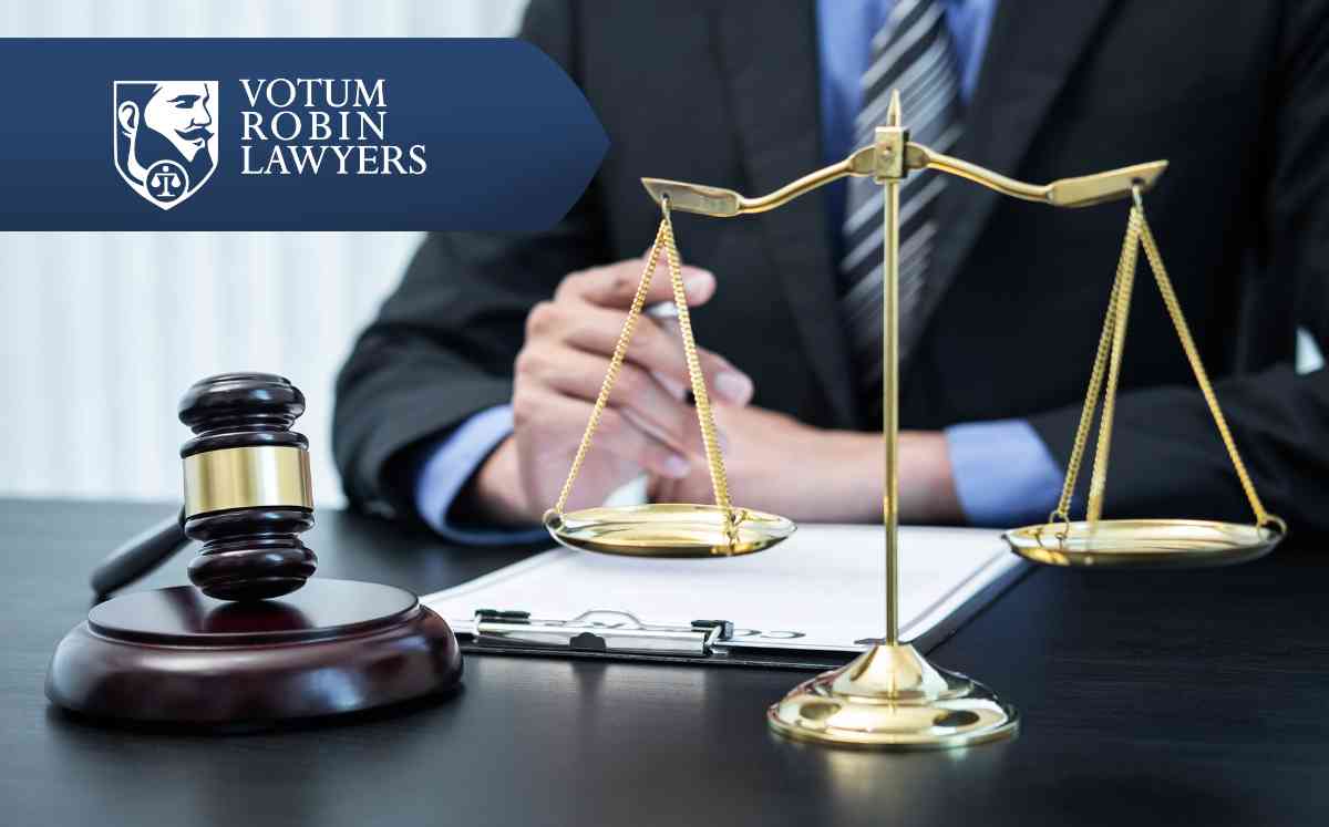 Two lawyers in suits review documents on a desk with a gavel and scales of justice; law firm logo in the corner.