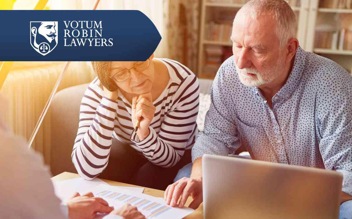 Two lawyers in suits review documents on a desk with a gavel and scales of justice; law firm logo in the corner.