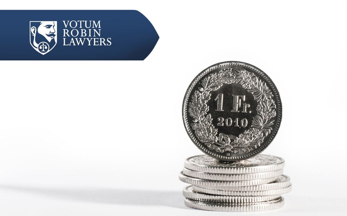 Two lawyers in suits review documents on a desk with a gavel and scales of justice; law firm logo in the corner.